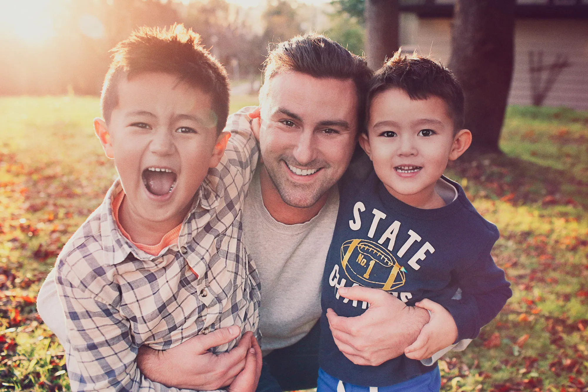 Joyful father and two sons embracing outdoors in golden light, one boy laughing. SixSixty Studio Singapore.