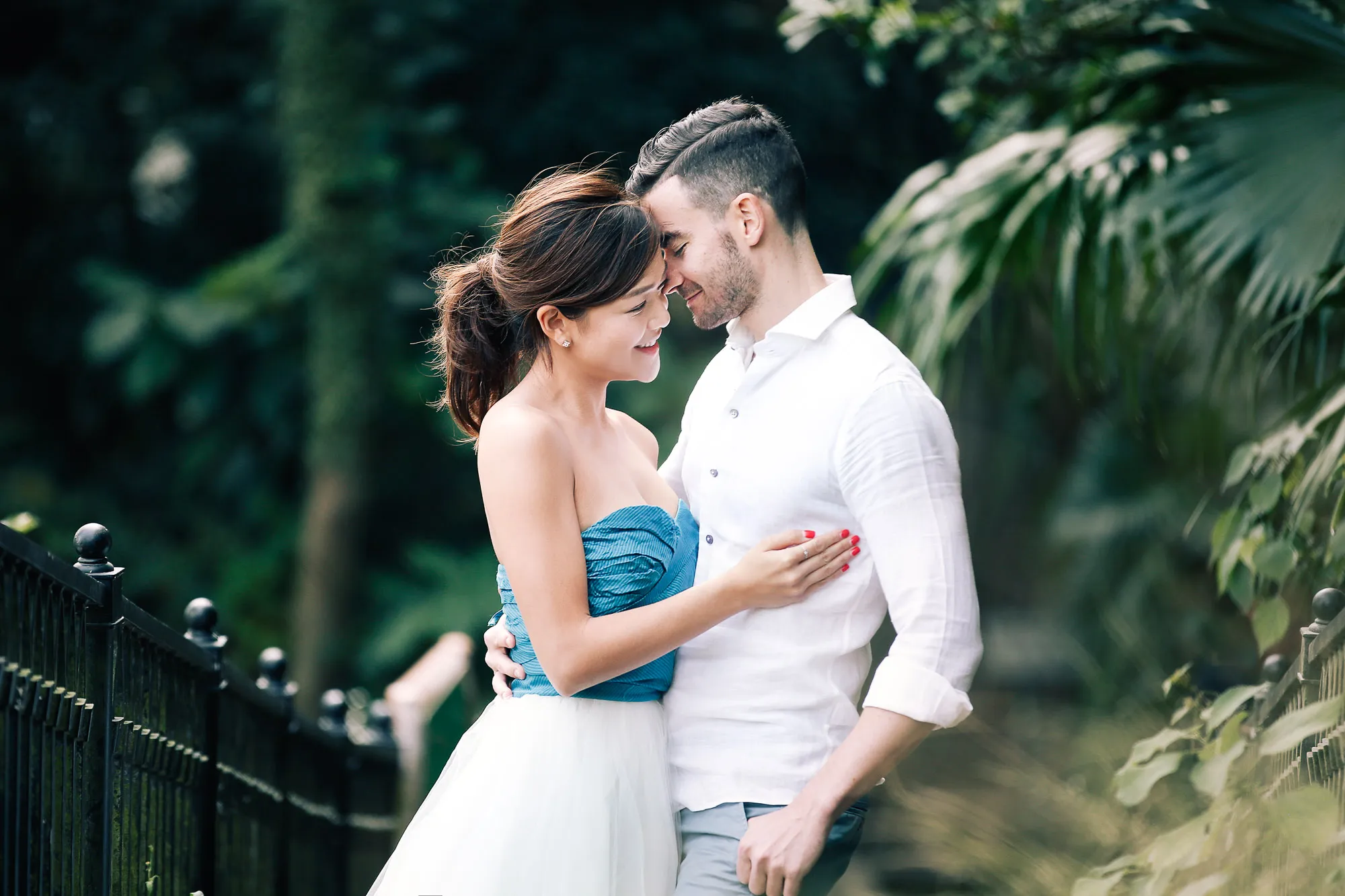 Romantic photo of a smiling couple embracing in a lush green park, foreheads touching.