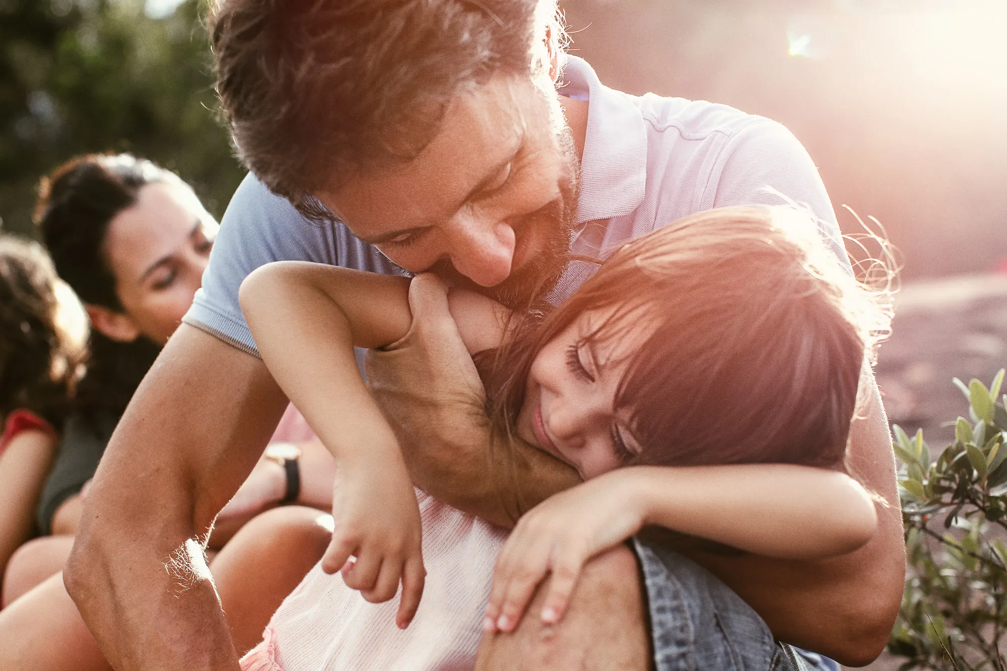 A father lovingly hugs his daughter outdoors, bathed in warm, golden sunlight. SixSixty Studio Singapore.