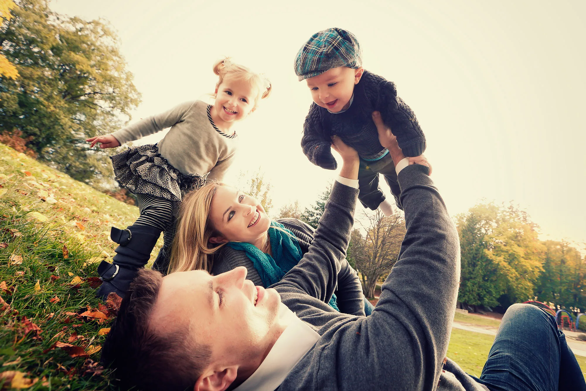 Happy family of four playing in an autumn park. Dad lifts baby, mom and daughter smile.