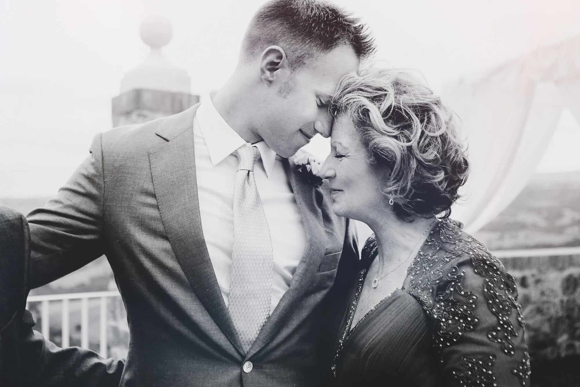 SixSixty Studio photo: Man in suit and woman share a tender, intimate moment, foreheads touching, eyes closed, outdoors.