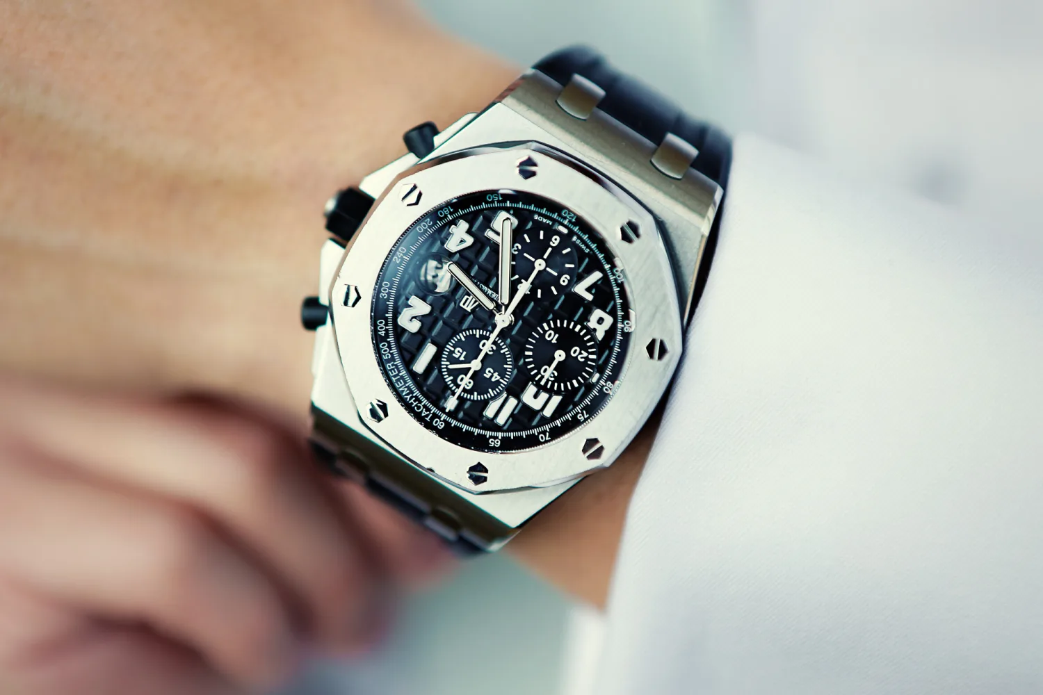 Close-up of luxury chronograph watch with steel case and black dial worn on wrist.