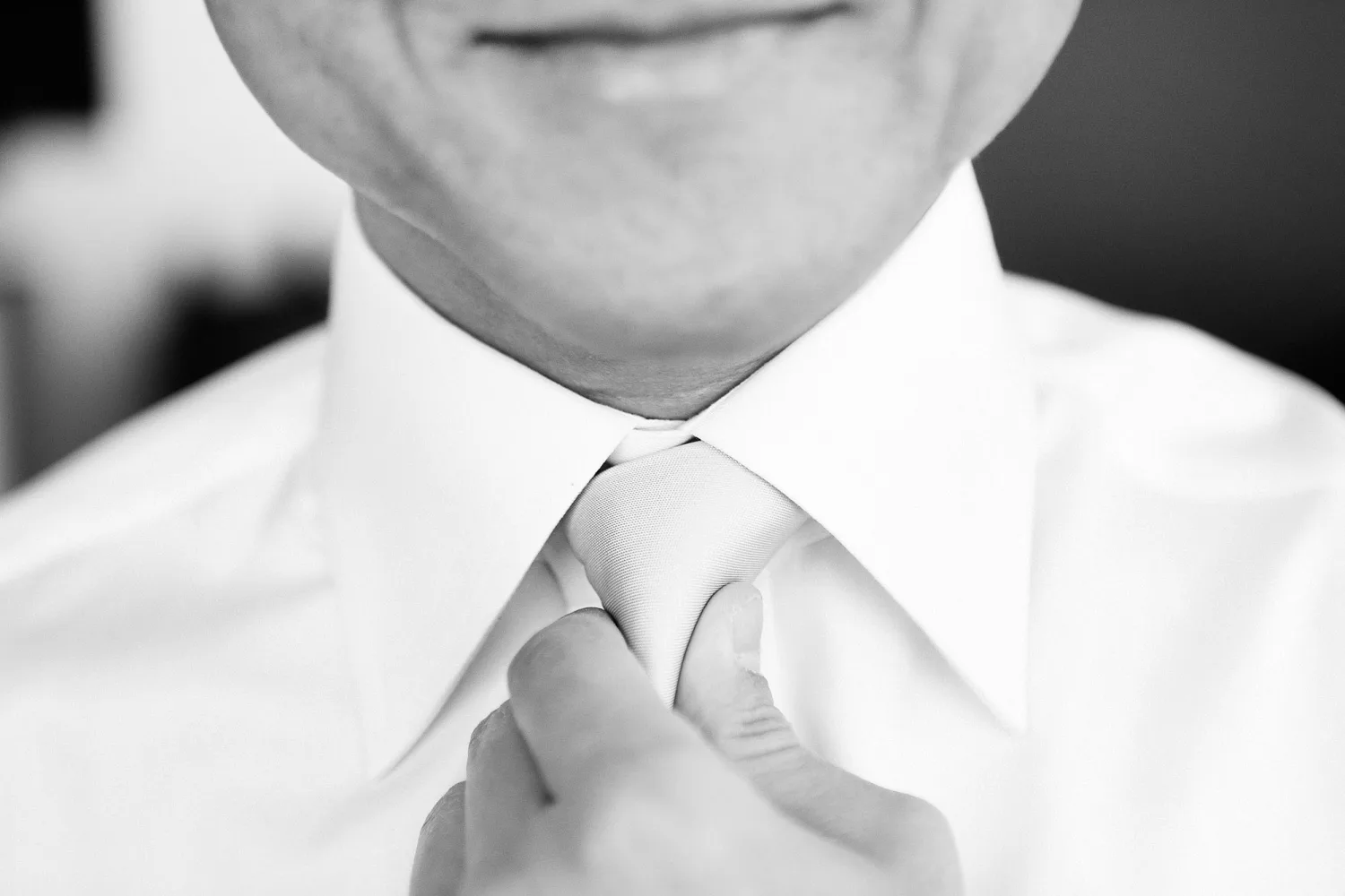 Close-up of groom adjusting white dress shirt and tie knot.