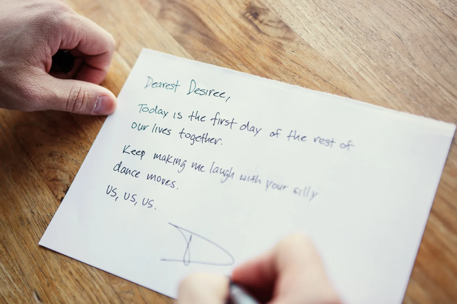Handwritten letter on white paper held over wooden surface with blue ink text.