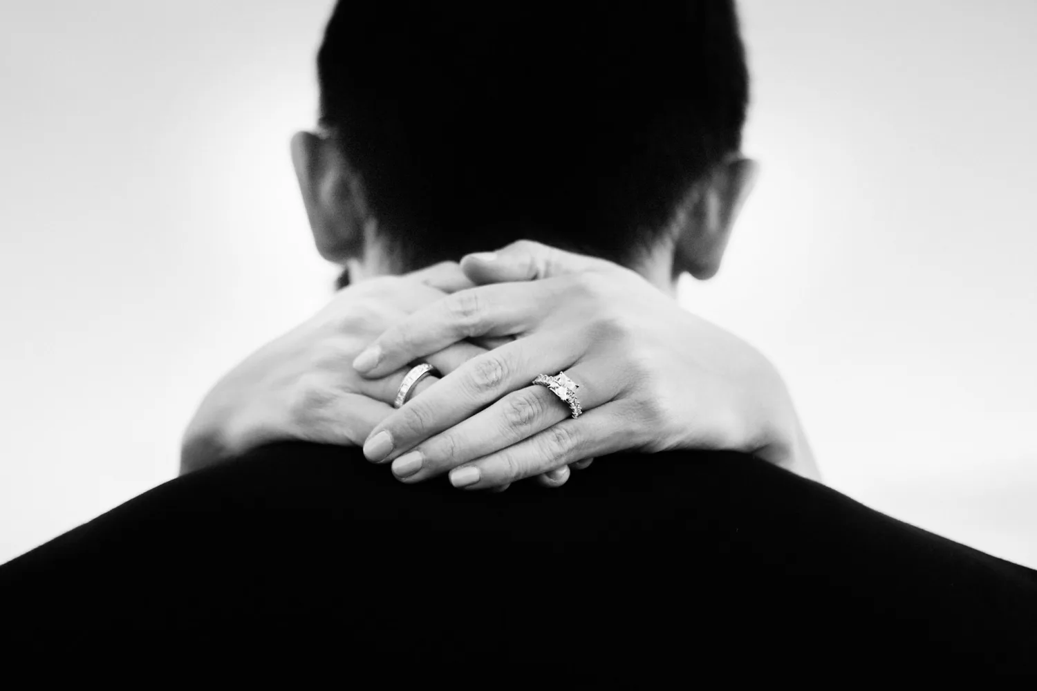 Hands displaying wedding rings resting on person's shoulder in black and white portrait.