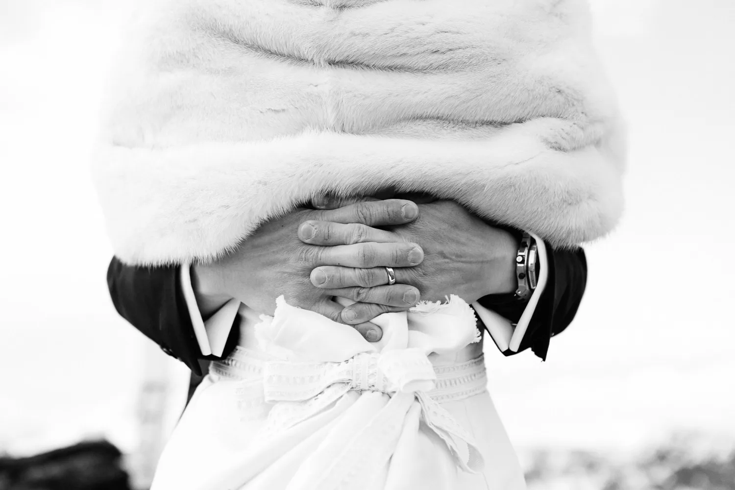 Hands with wedding rings displayed under white fur stole and formal attire.