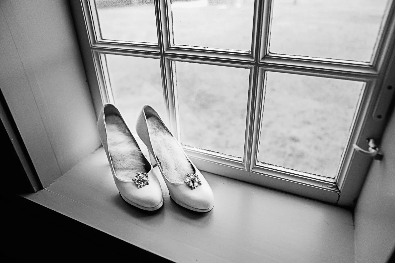 White bridal shoes with jeweled ornaments on windowsill in black and white.