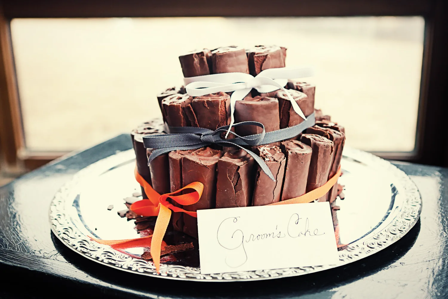 Tiered chocolate cake with ribbon bows on ornate plate labeled 'Groom's Cake'