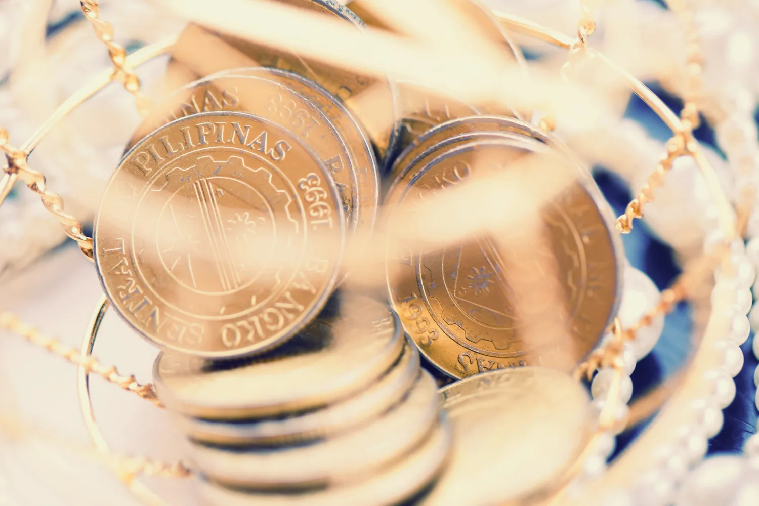 Close-up of Philippine peso coins suspended on gold chains with white beaded details.