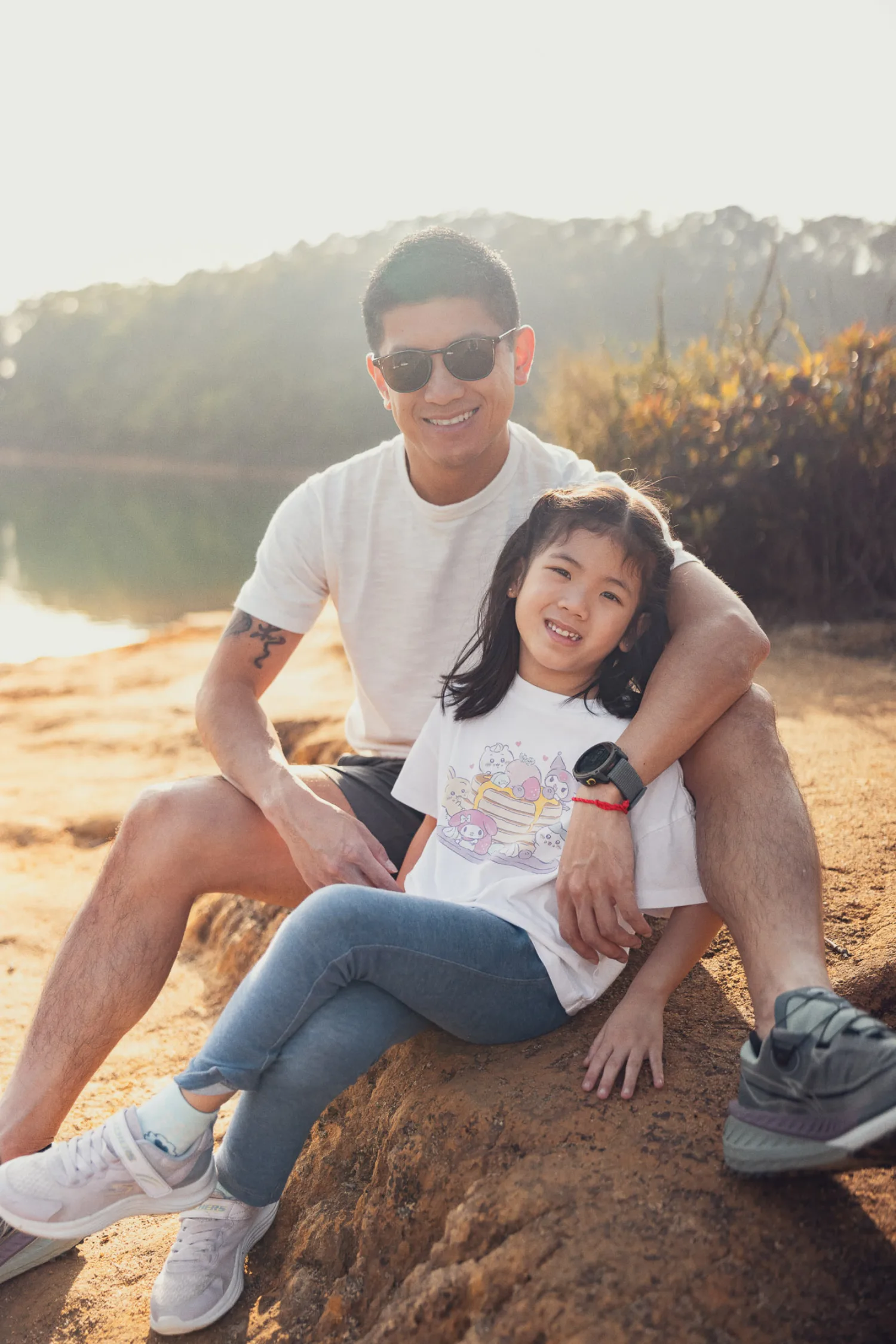 Lok and Leila sitting together by the tranquil reservoir, smiling in the warm light