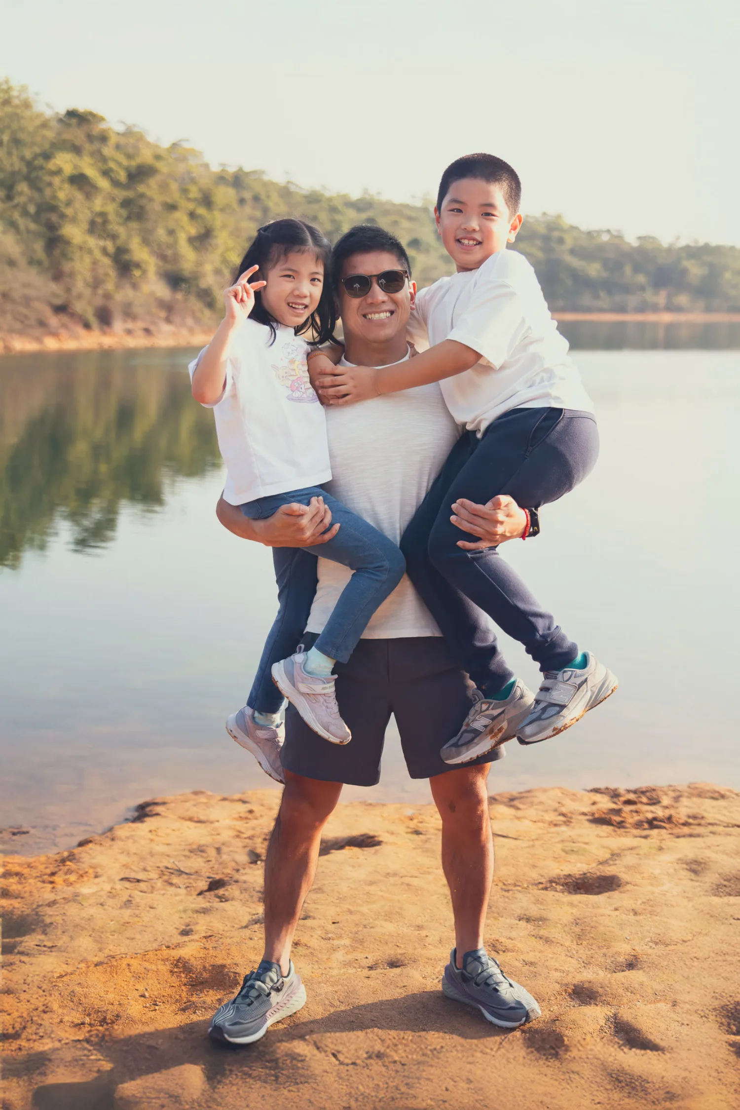 Lok carrying both Lachlan and Leila on his hips by the reservoir, everyone laughing
