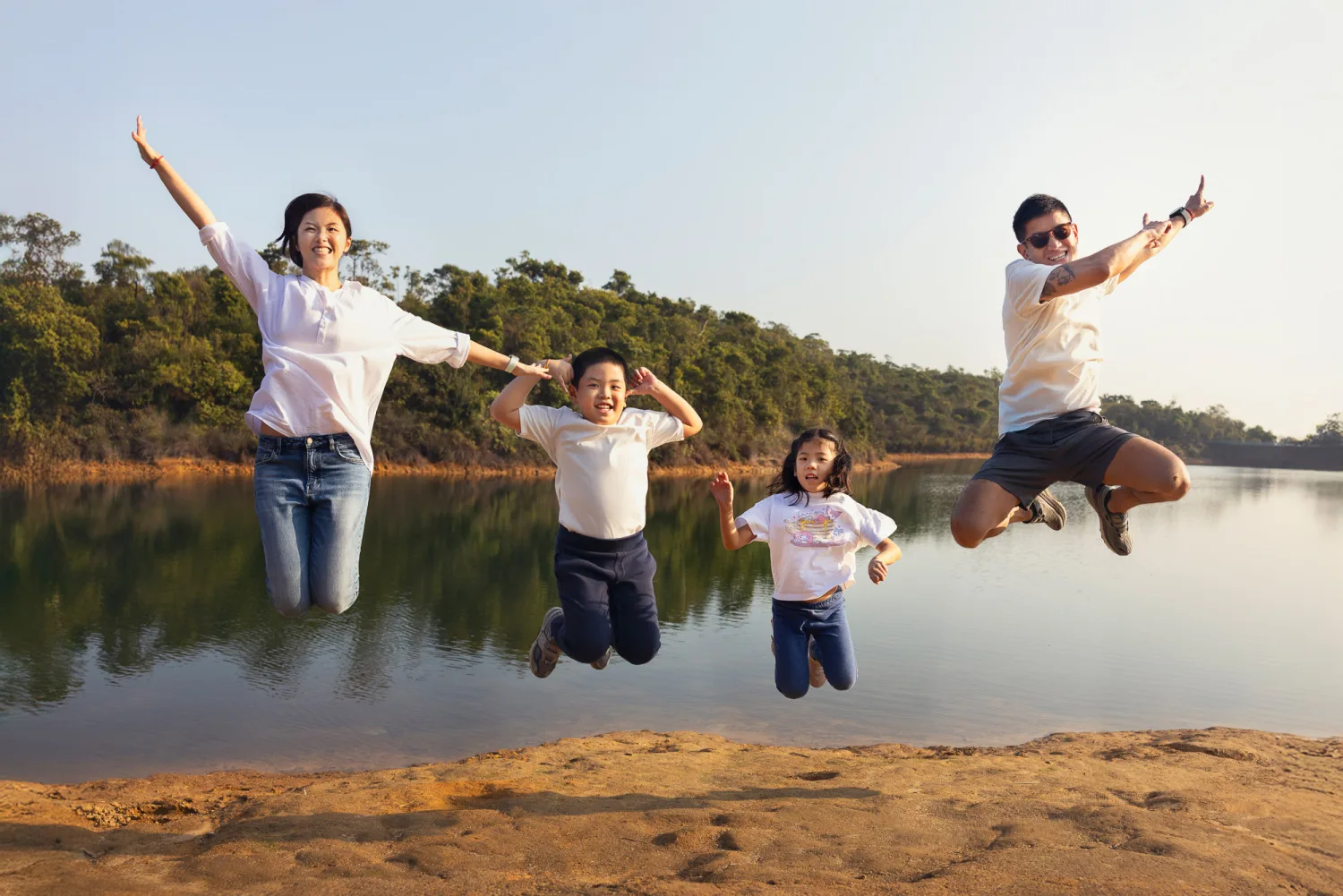 The whole family jumping in the air by the reservoir, arms raised and beaming