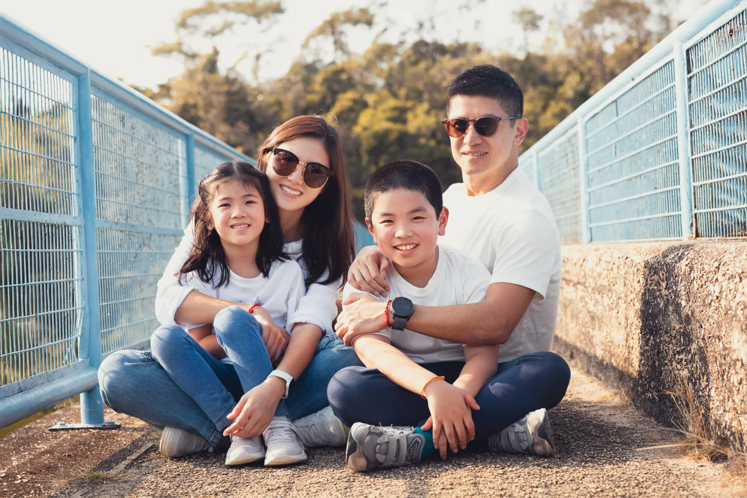 Family of four sitting together on a hiking bridge with green hills behind them