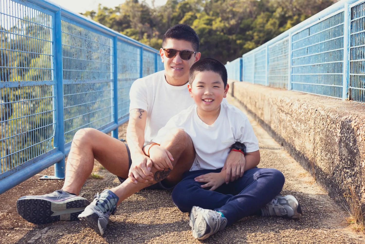 Lok and Lachlan sitting side by side on the hiking bridge, father and son sharing a warm embrace