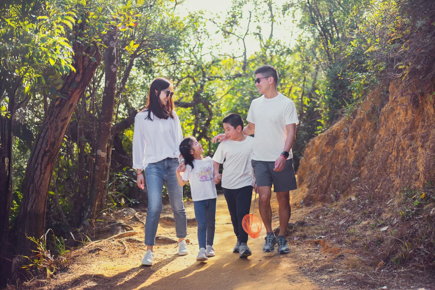 The family walking together along a sunlit Hong Kong forest trail, Lachlan leading with his arm around Leila