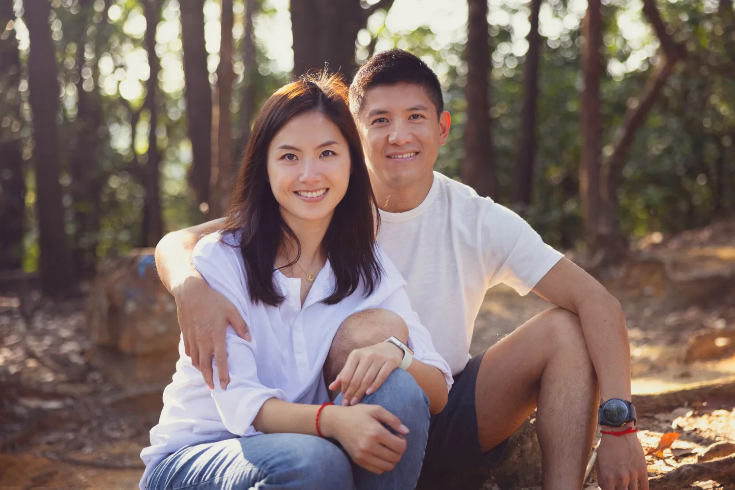 Xenia and Lok sitting together on the forest floor, smiling warmly in dappled sunlight
