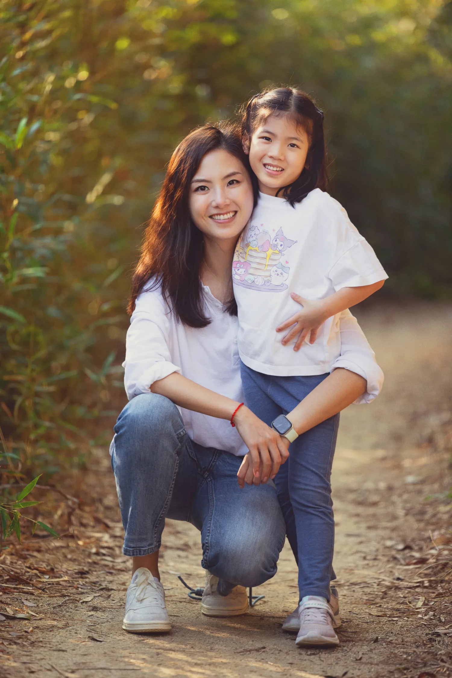 Xenia crouching to hug Leila on a leafy trail in golden afternoon light