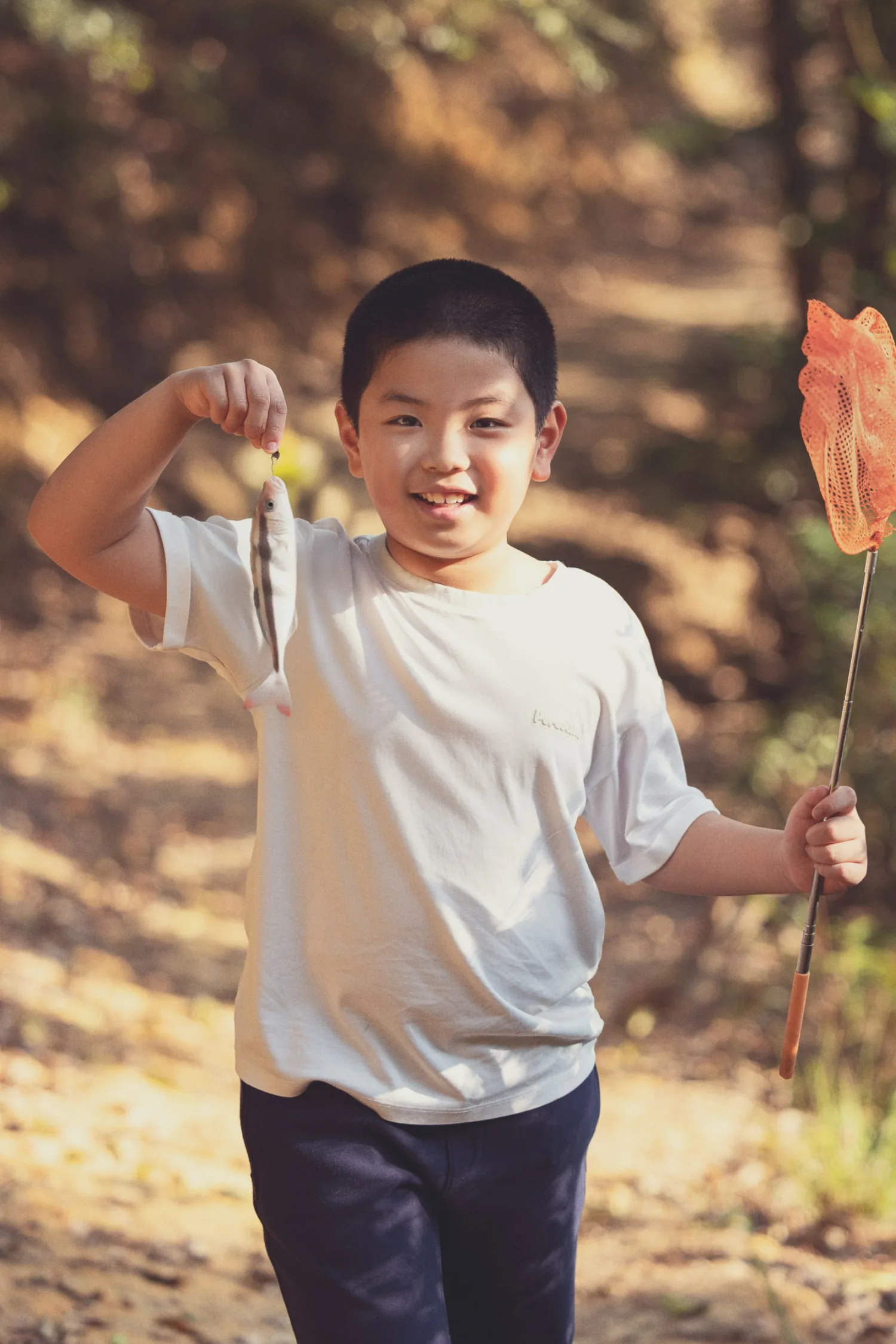 Lachlan proudly holding up a small fish he caught, grinning with delight in the forest