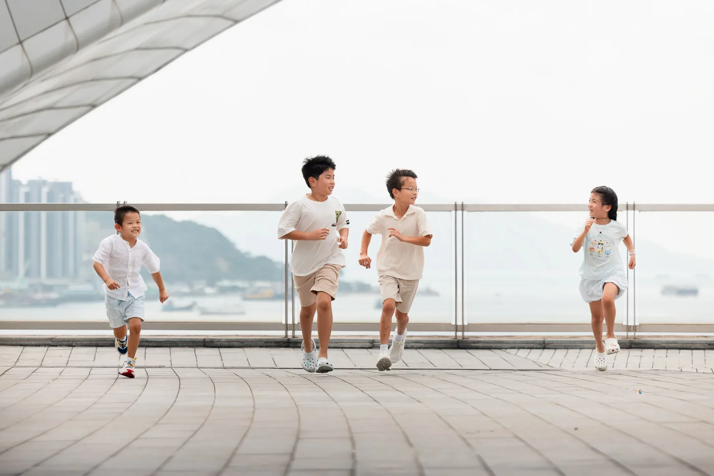 Four children running along the Hong Kong waterfront during a family friends session