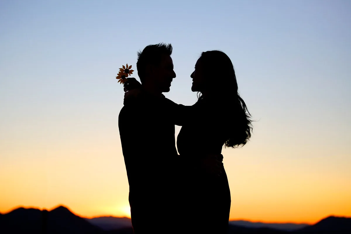 Julie and James silhouetted against a Joshua Tree sunset with a single flower
