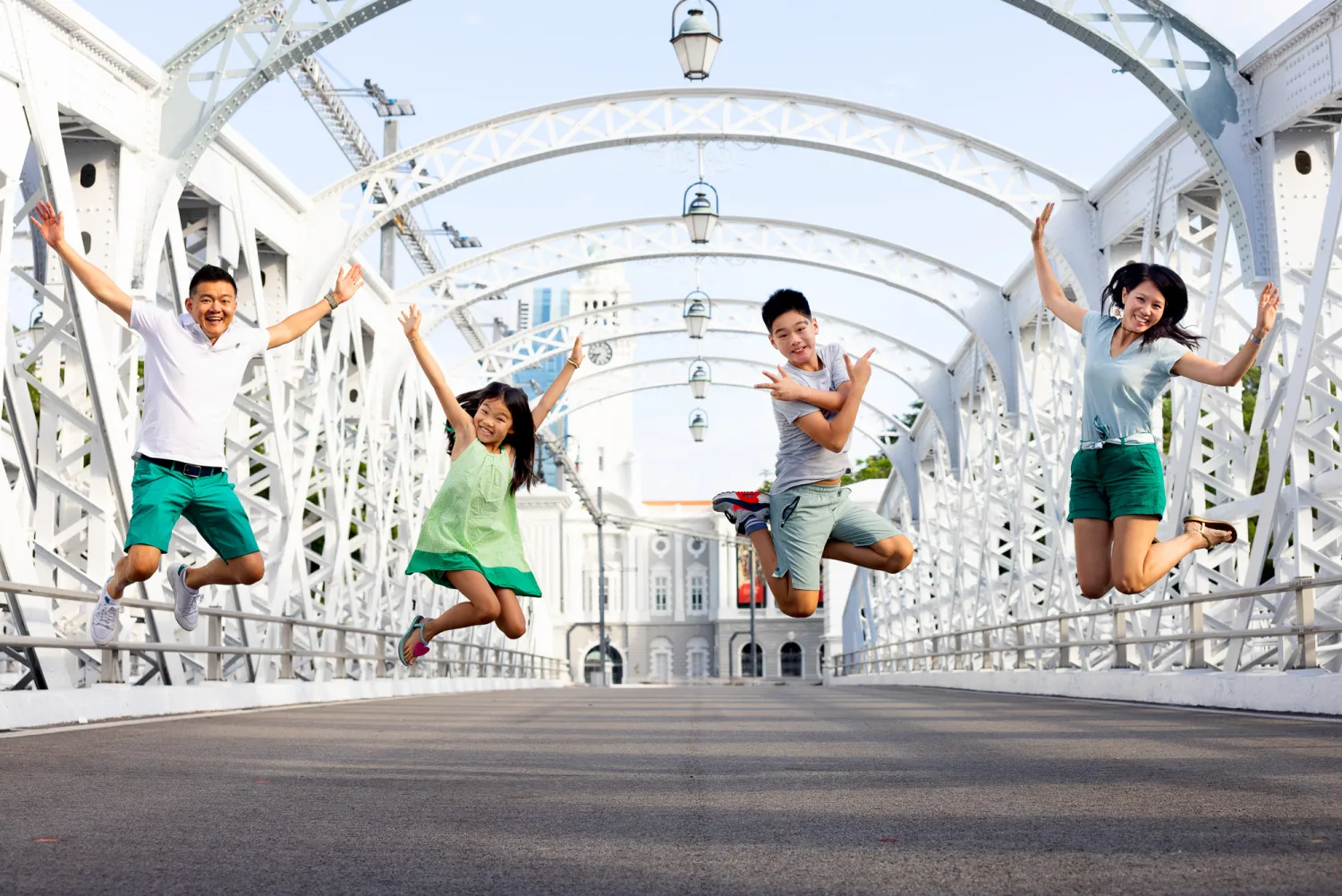 The whole family jumping mid-air on an ornate white bridge, arms raised and beaming