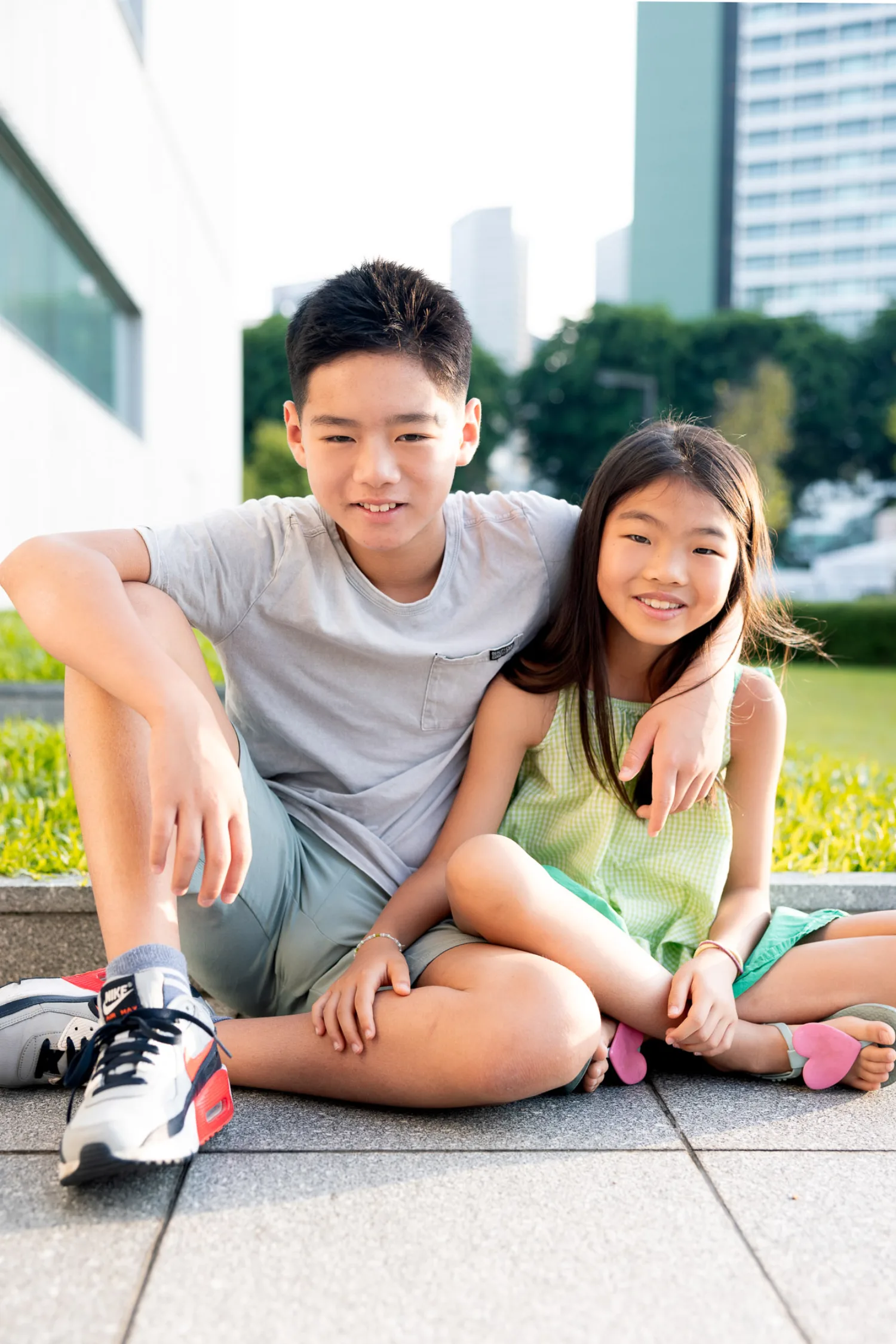 Avery and Mirei sitting side by side on a sunlit walkway with Singapore's skyline behind them
