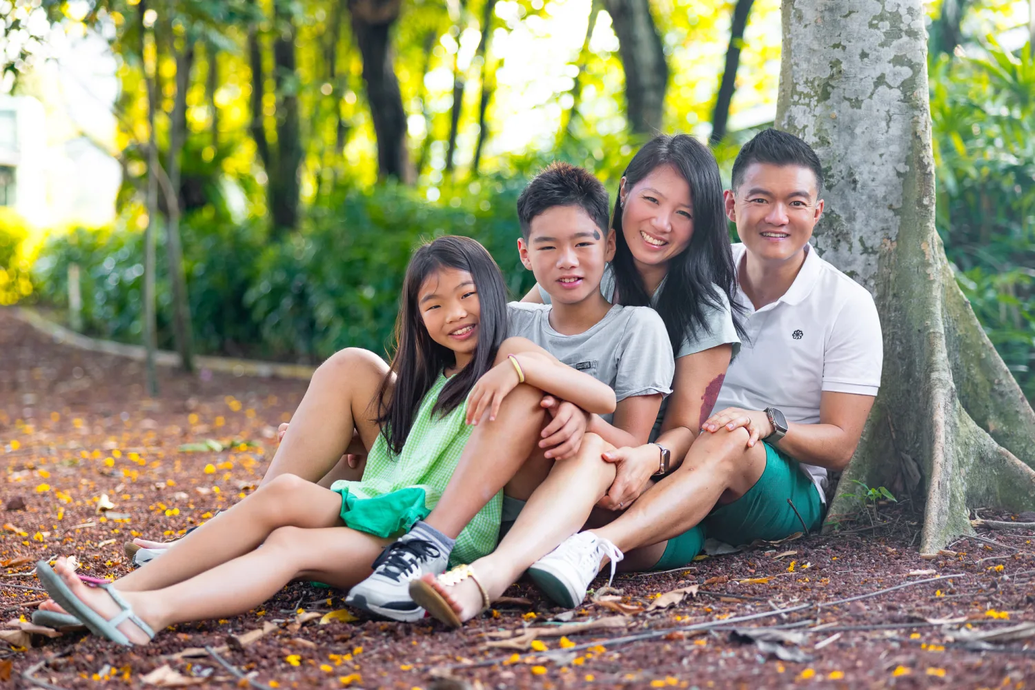 The family sitting together under a large tree, relaxed in warm dappled sunlight