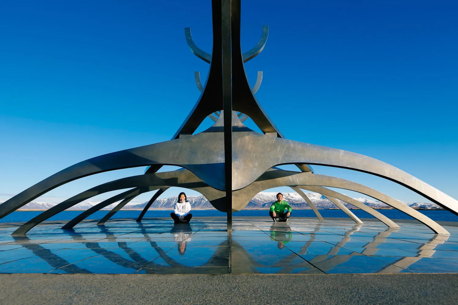 Desiree and Derek beneath the Sun Voyager with Reykjavik harbour and mountains behind them