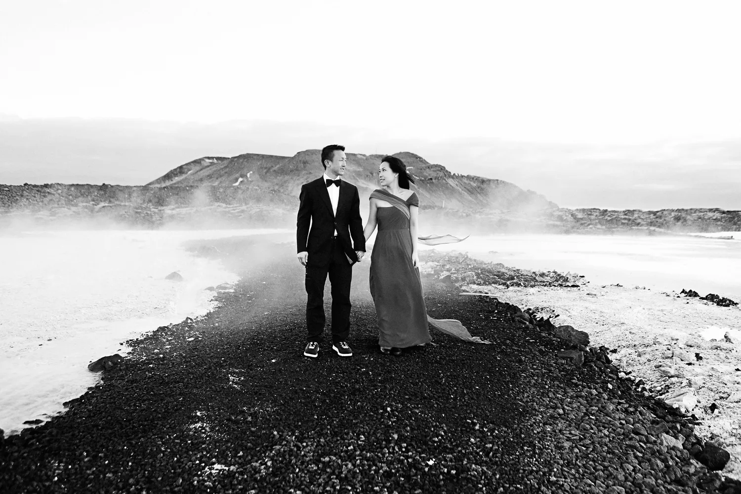 Desiree and Derek holding hands in formalwear in Iceland's cold, misty landscape