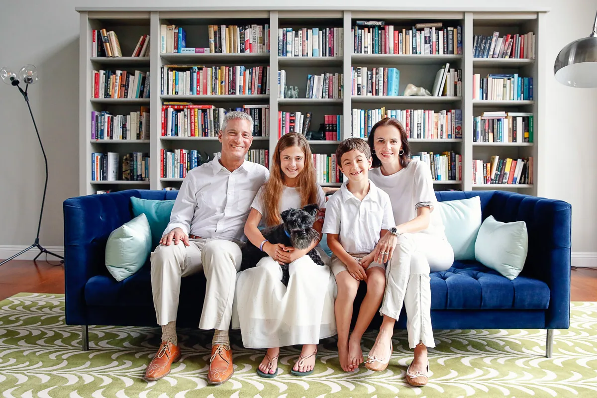 Rob, Clara, Jess and Hannah with their dog on a blue sofa in front of bookshelves at home in Singapore