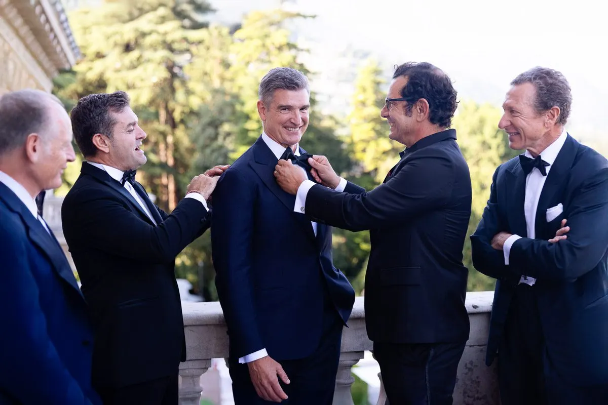 Emilio and his groomsmen in navy tuxedos, sharing a laugh as they adjust his bow tie