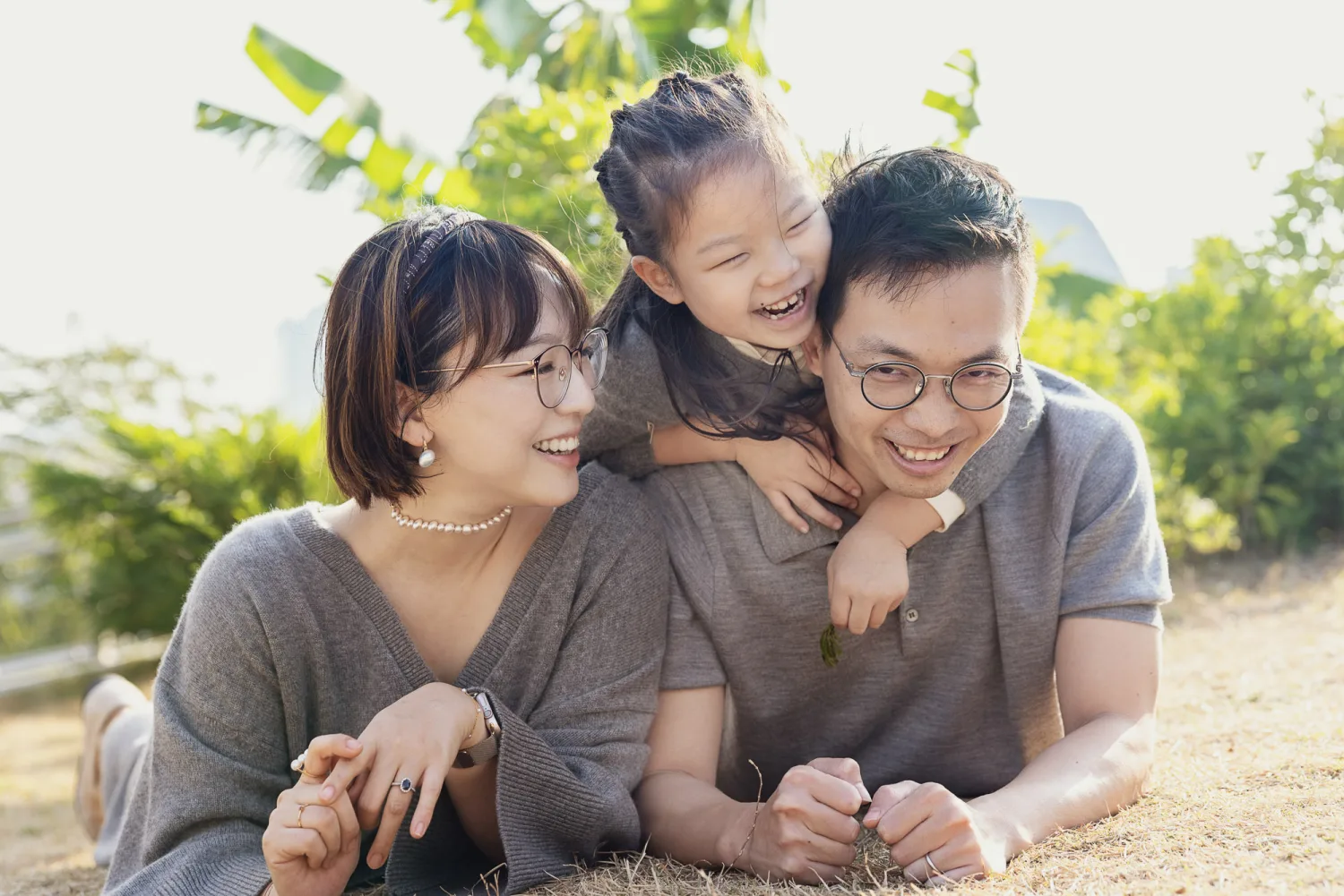 Emma playfully tackling Vincent from behind on the grass while the whole family laughs at West Kowloon