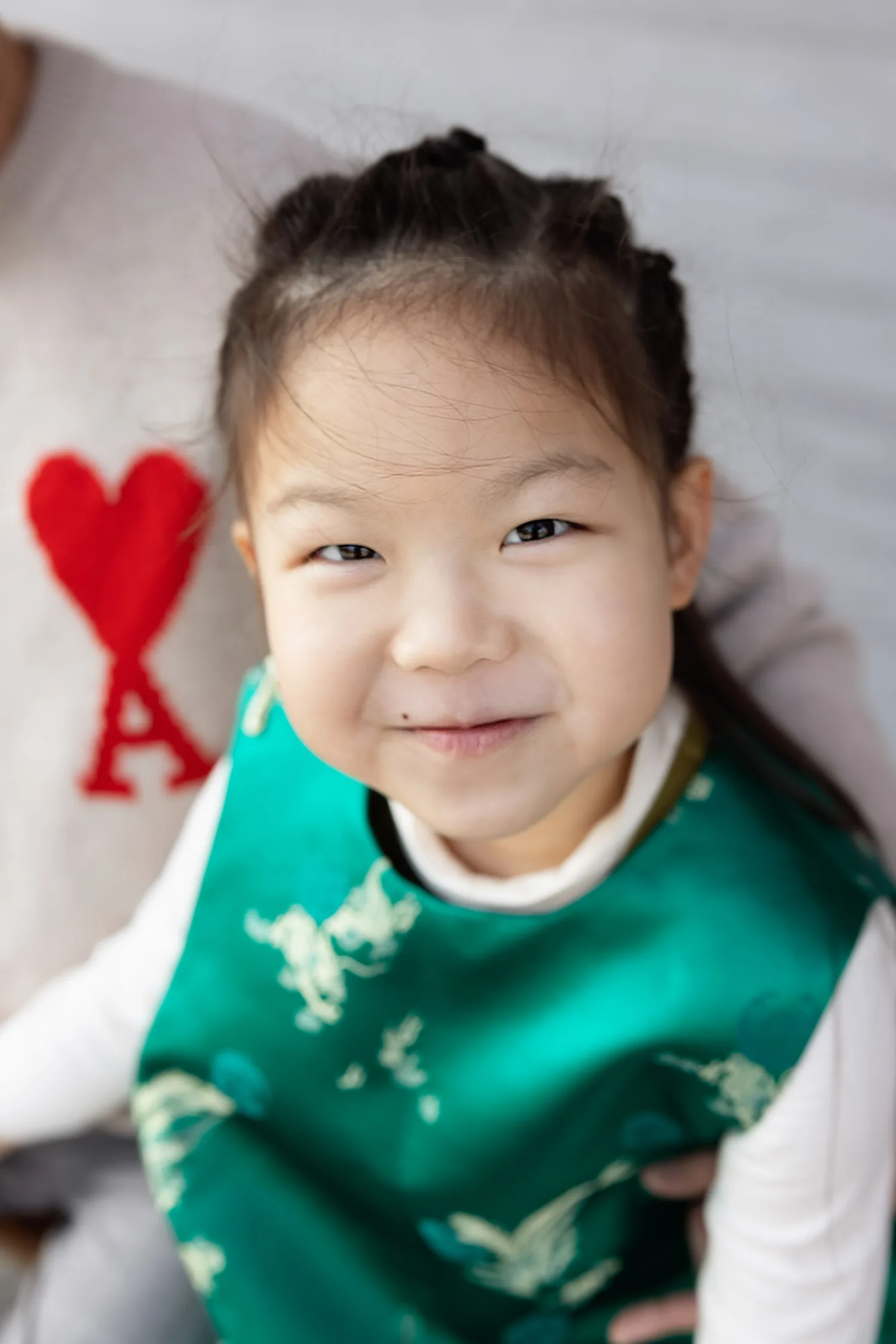 Emma smiling sweetly at the camera in her emerald green patterned dress, Vincent visible behind her in his heart-logo sweater
