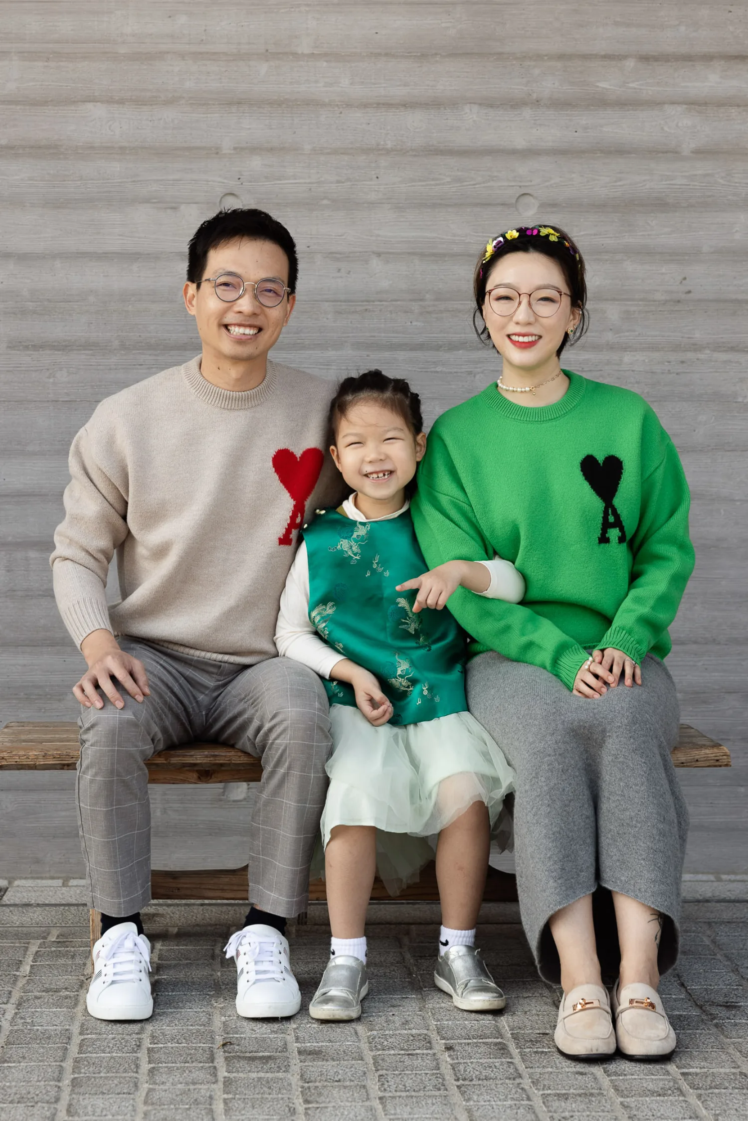 Bonnie, Vincent and Emma seated on a wooden bench, all smiling — parents in matching heart sweaters, Emma between them