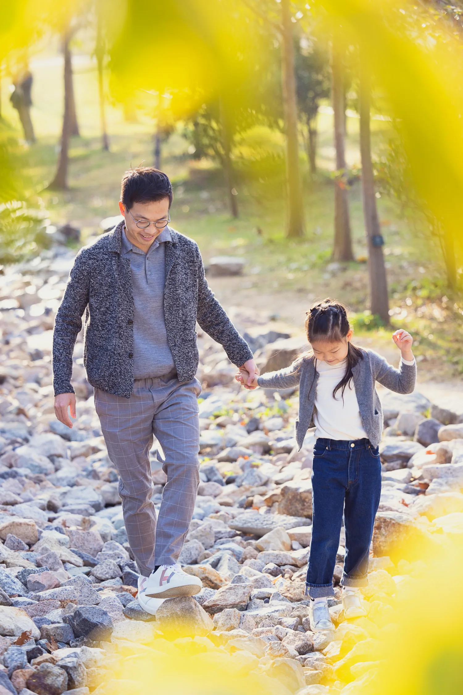 Vincent and Emma walking hand-in-hand over the rocky waterfront at West Kowloon, carefully picking their way across the uneven ground