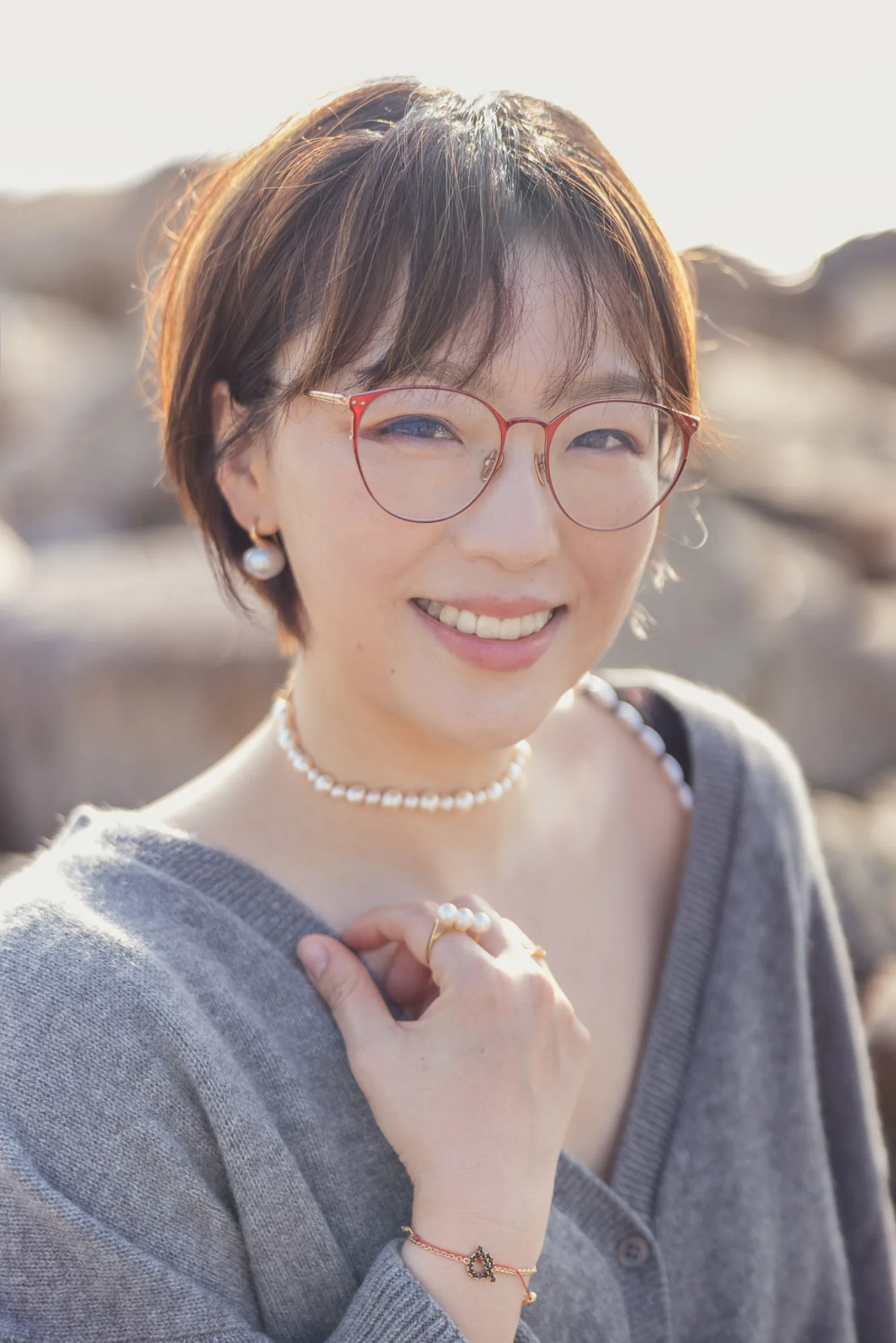 Bonnie smiling in warm natural light at West Kowloon, wearing grey cardigan with pearl necklace and earrings