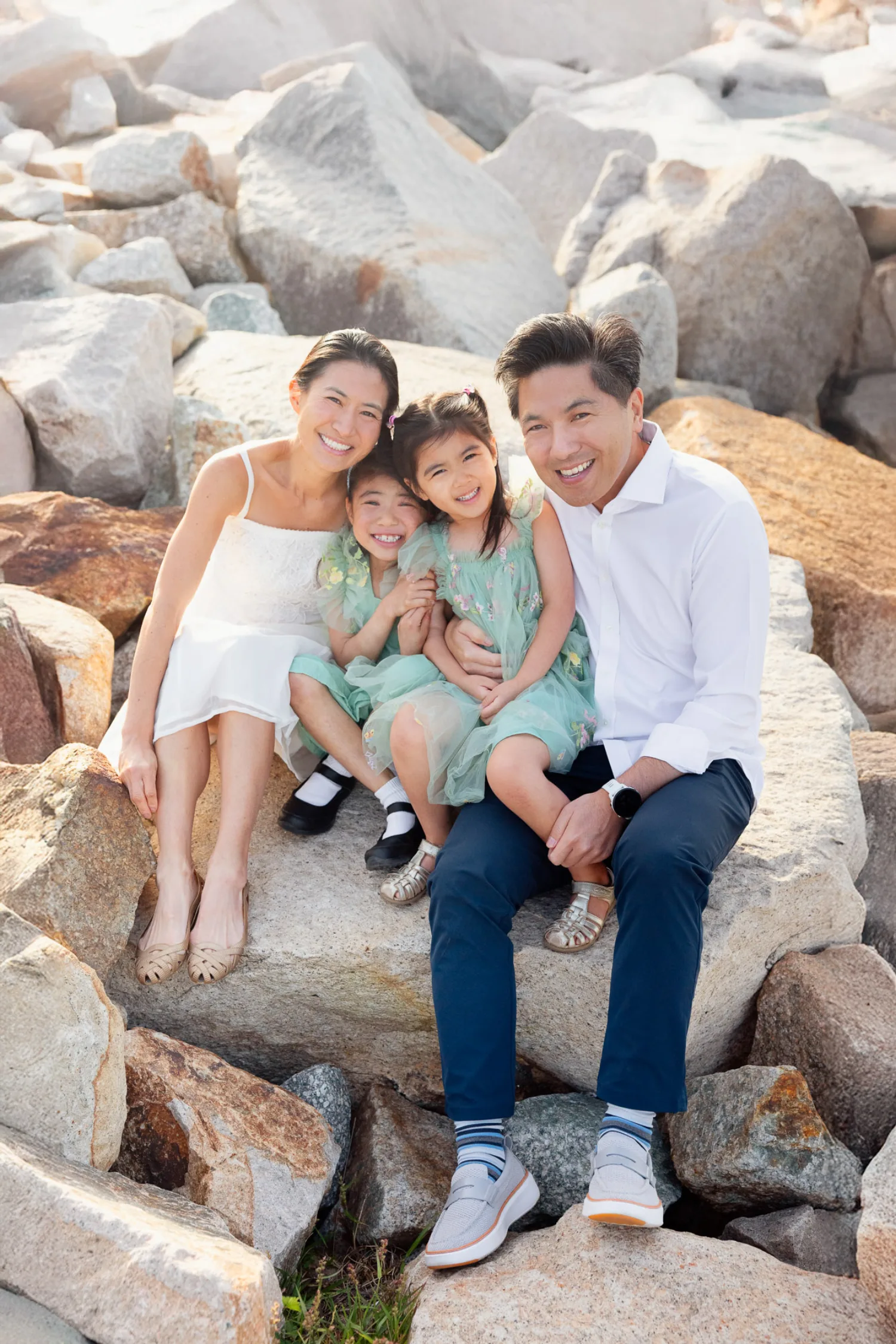 Terence, Suzanna, Sophie, and Zoe sitting together on the rocks with Hong Kong skyline behind them at sunrise