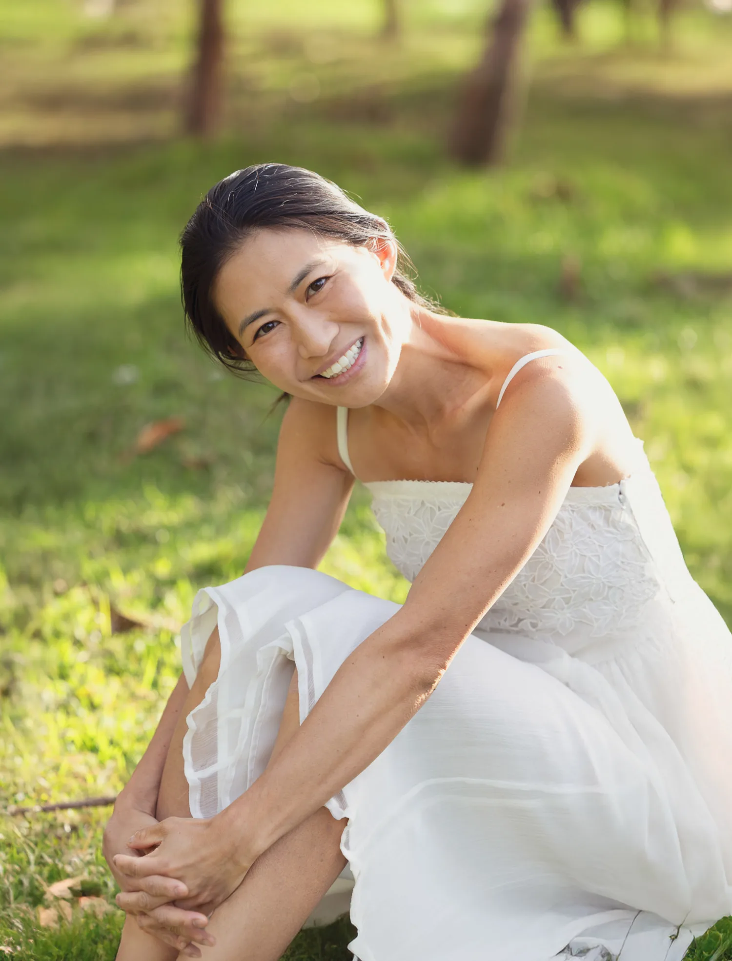 Suzanna smiling joyfully in a white dress on the sunlit grass at West Kowloon