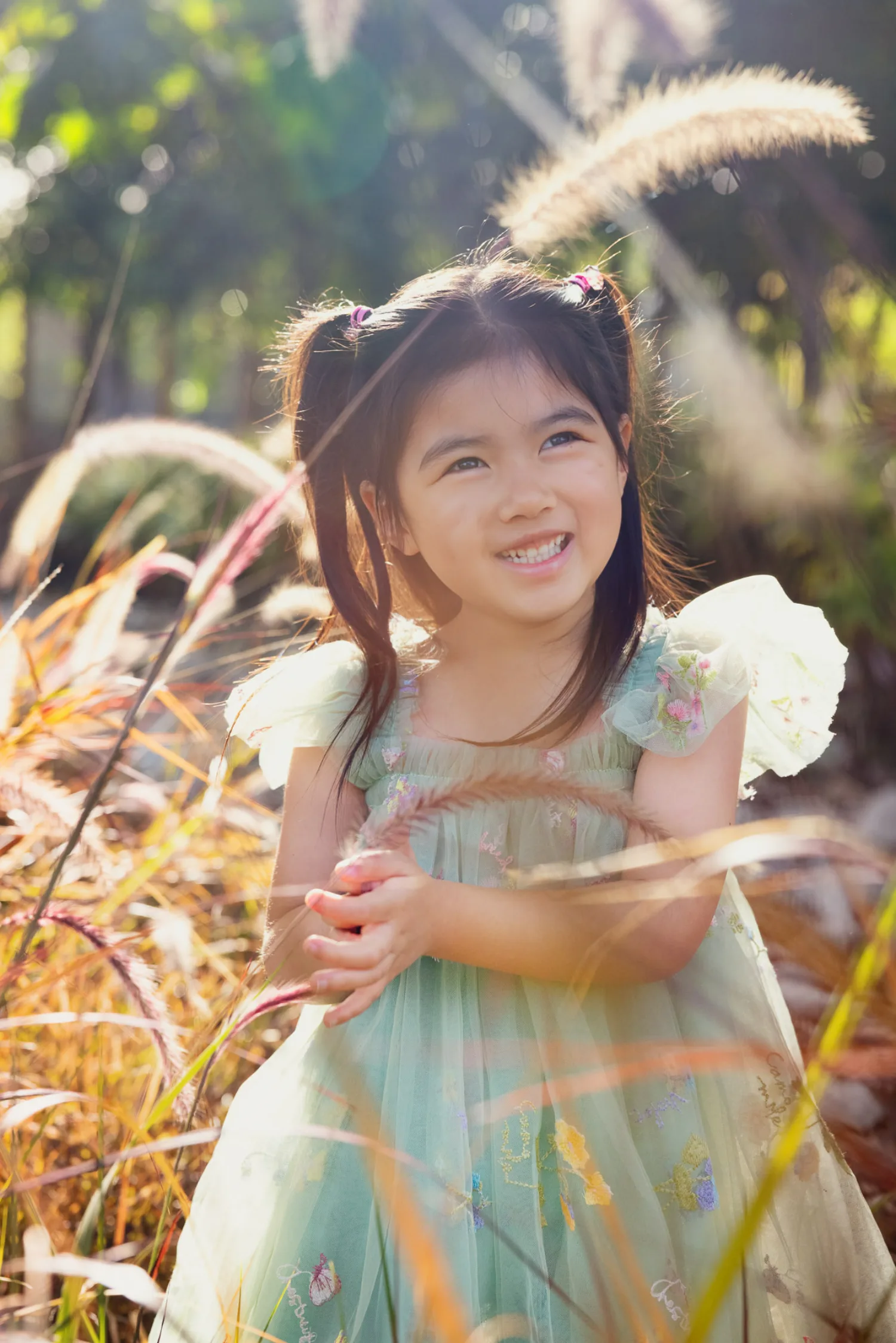 Zoe standing among tall feathery grasses, smiling upward in soft golden light