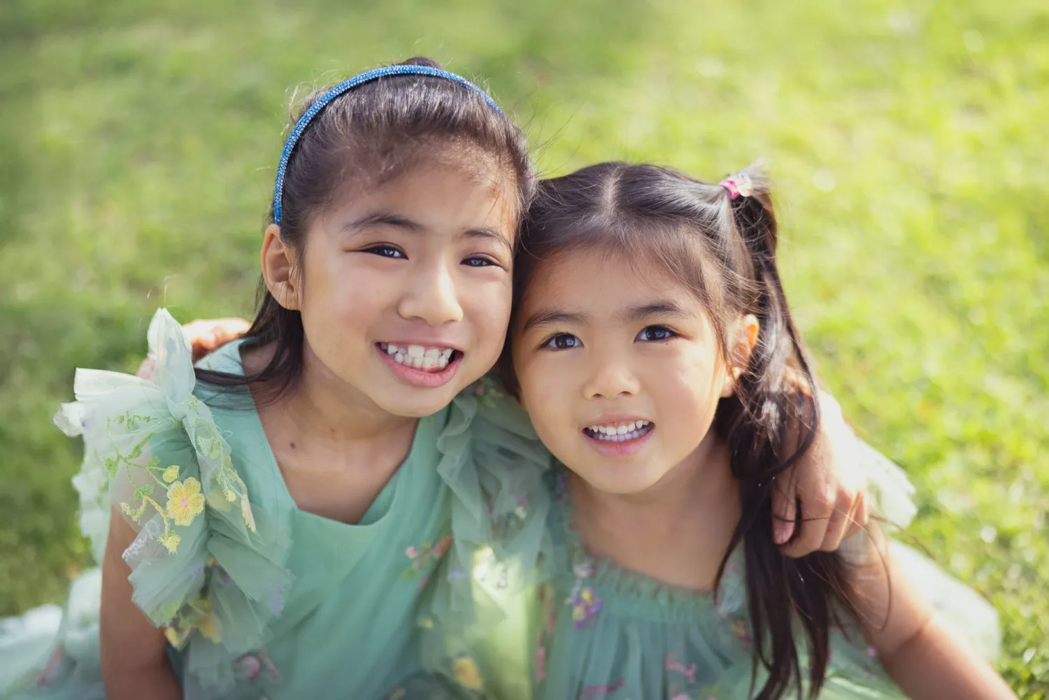 Sophie and Zoe side by side in matching mint green dresses on the sunlit lawn