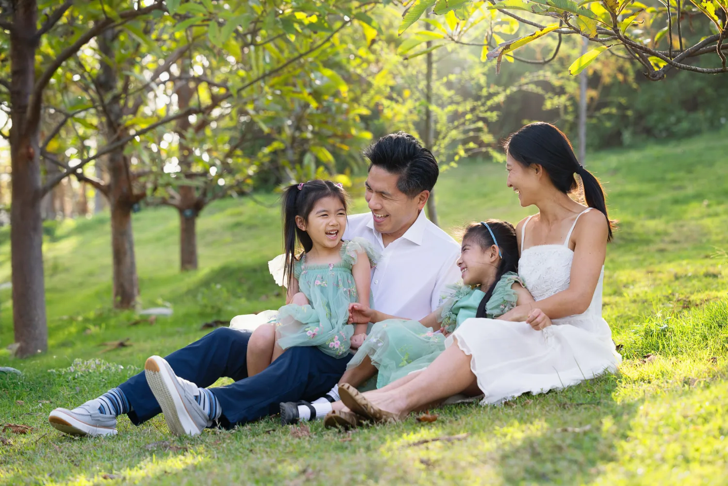 Terence, Suzanna, Sophie, and Zoe sitting on a grassy slope sharing a laugh