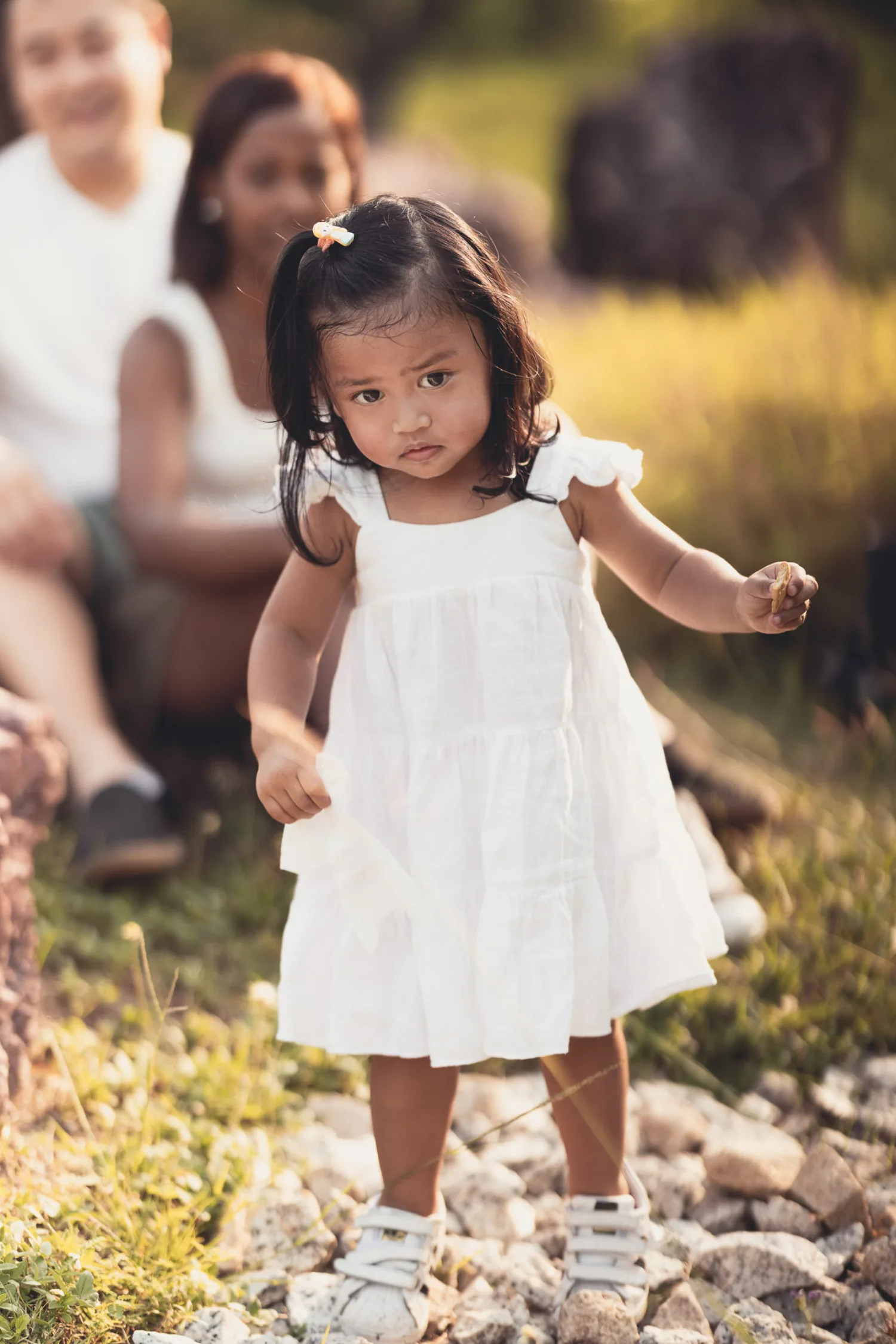 Gabby standing thoughtfully on a path as her parents rest behind her